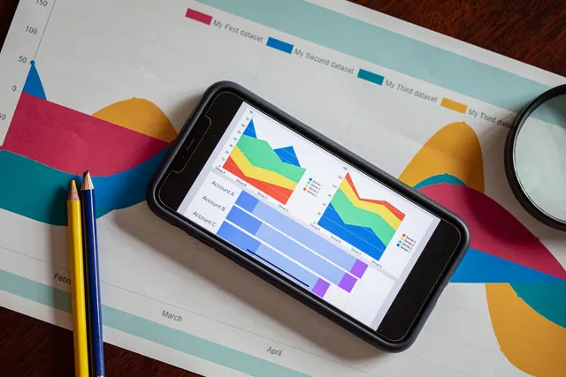 Overhead view of a smartphone displaying colorful charts on paper graphs, symbolizing mobile data analysis. Reporting: what beginners should know in 2027
